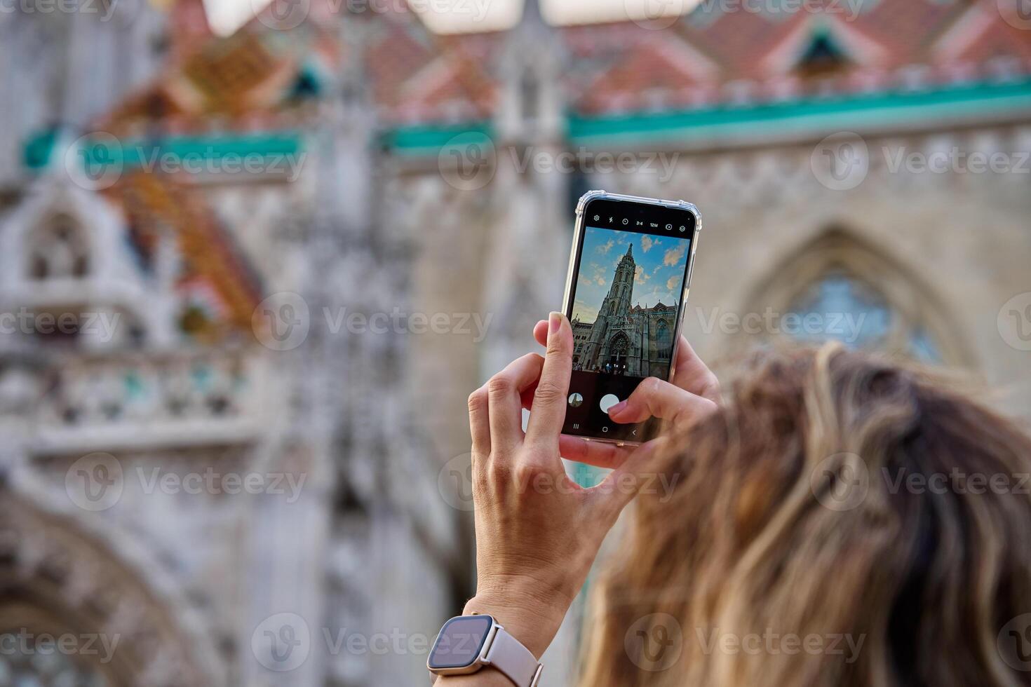 Female tourist capturing photo of historic cathedral in Budapest using smartphone. Traveler walking at city street