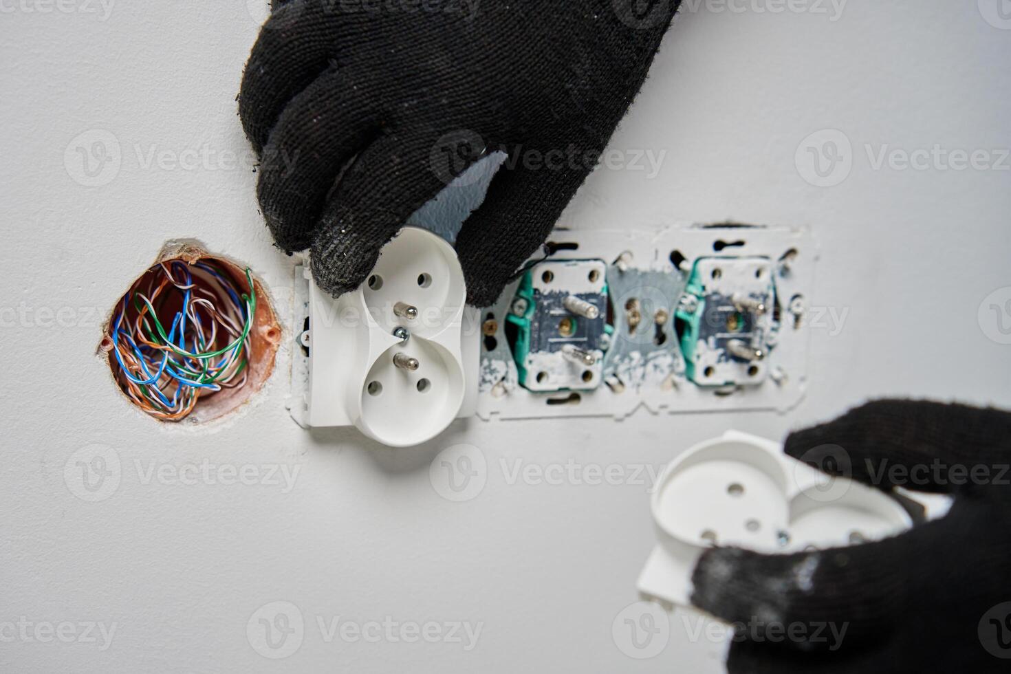 Close-up of an electrician wearing black gloves installing power socket on white wall. Electrical repair and maintenance process in progress photo