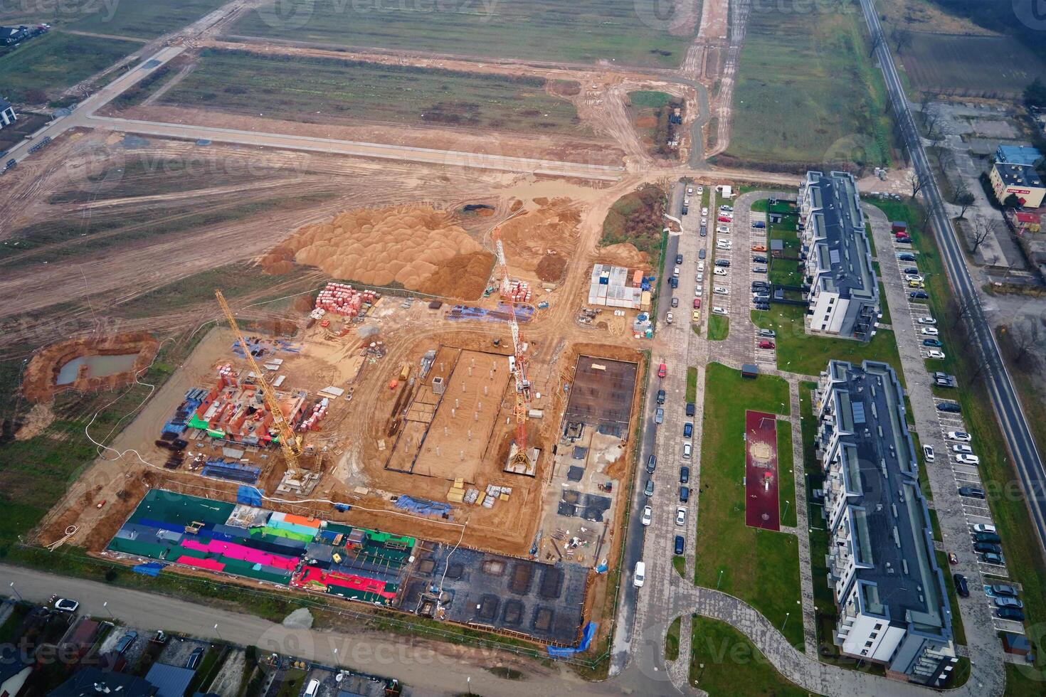 Aerial view of residential buildings under construction surrounded by completed homes and apartments. Cranes, foundations and building materials at construction site. New neighborhood in small town photo