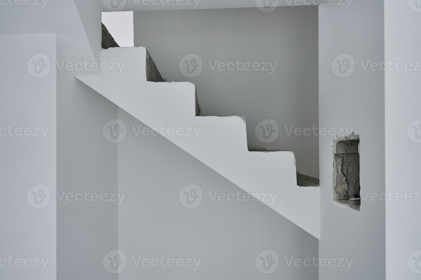 Unfinished concrete staircase in modern minimalist interior. New apartment with raw construction elements and white walls. Building under repair photo