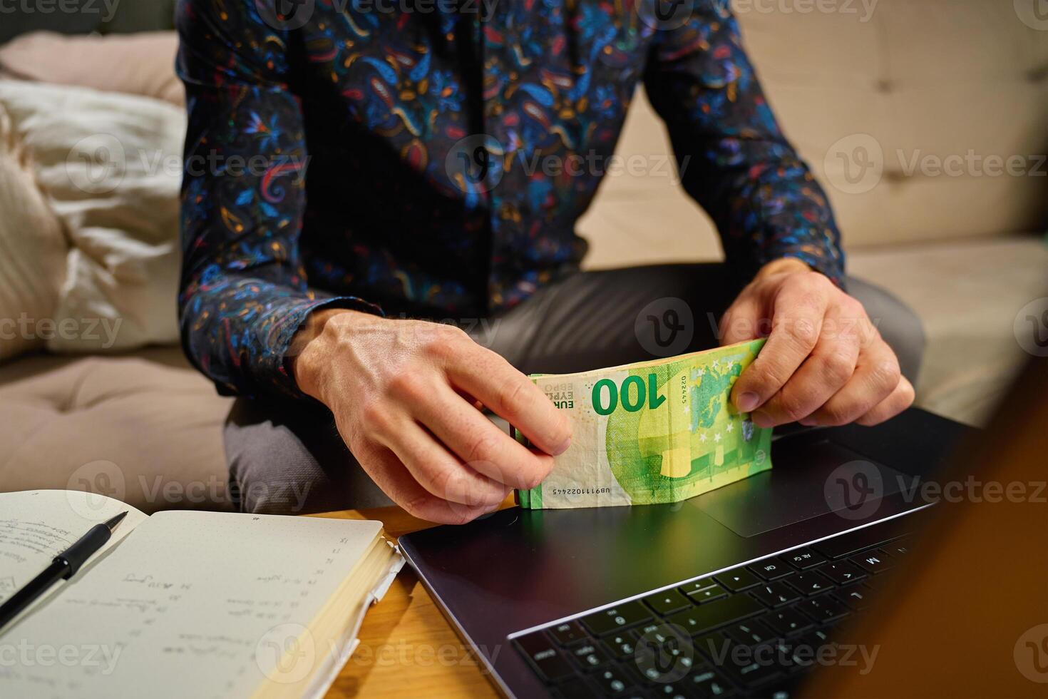 Man counting euro banknotes, sitting in front of table with laptop and notebook photo