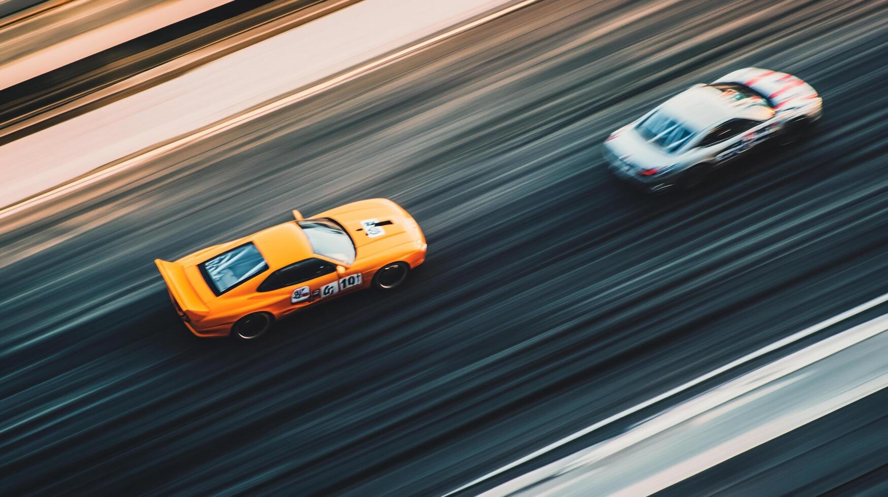 High-speed race cars compete neck and neck, motion blur emphasizing their blazing speed and competition. The orange car is slightly ahead. photo