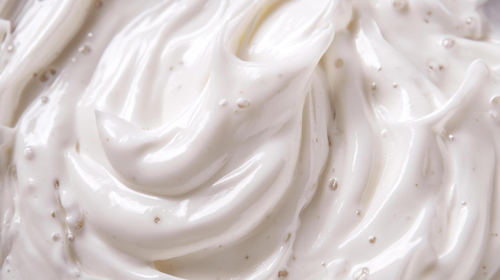 Close-up shot of thick, smooth, white cream. The cream is swirled and has a glossy texture. Tiny particles are visible in the cream. photo