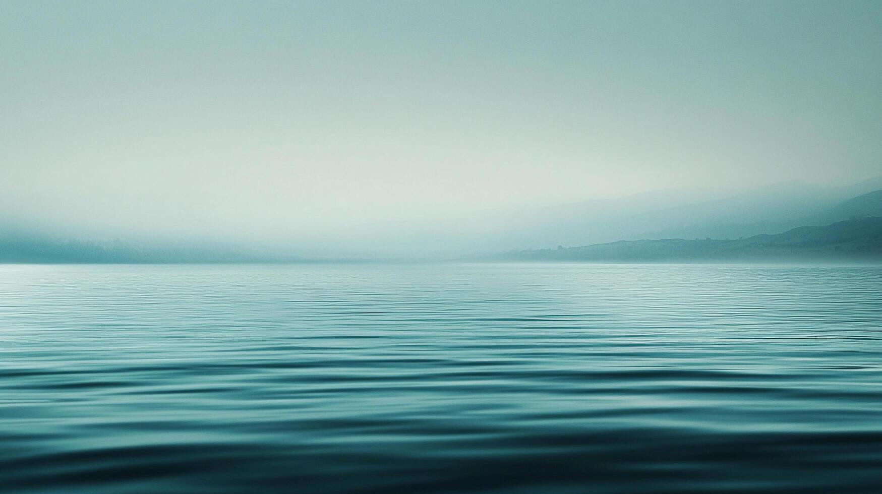 Serene turquoise landscape. Soft, misty mountains loom distantly over calm water rippling in the foreground. Quiet, peaceful, and scenic. photo
