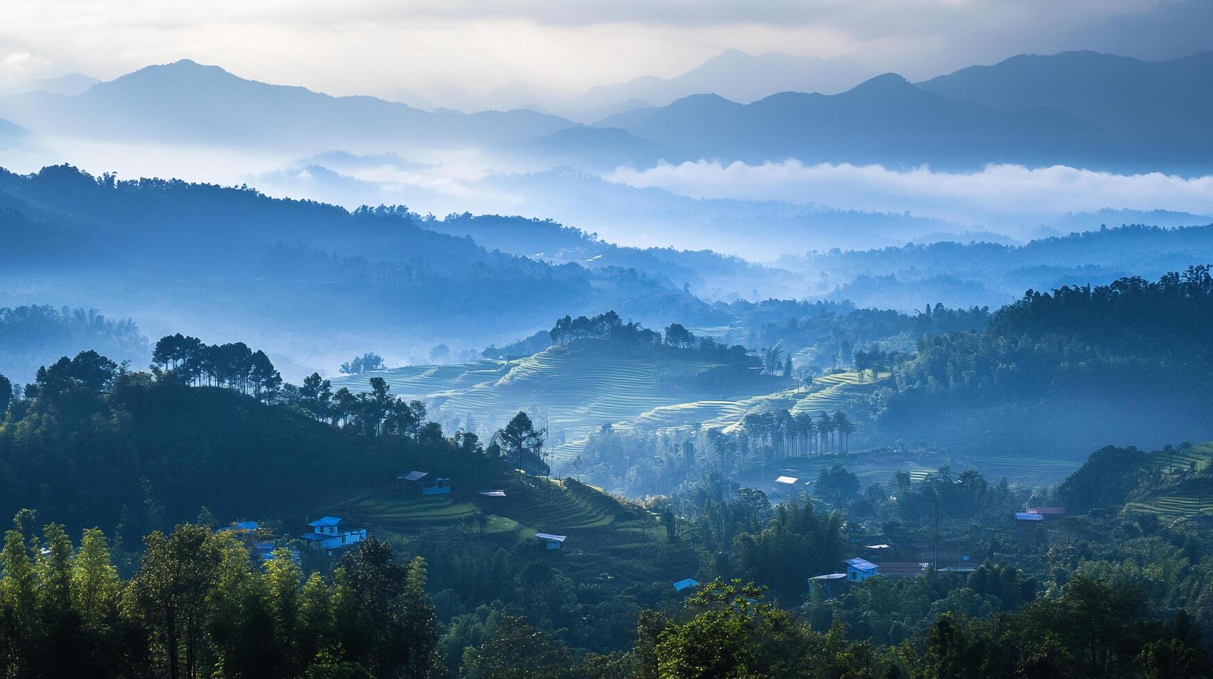 Misty mountains layered in blue hues create a serene landscape, with terraced fields and dwellings dotting the hillsides. photo
