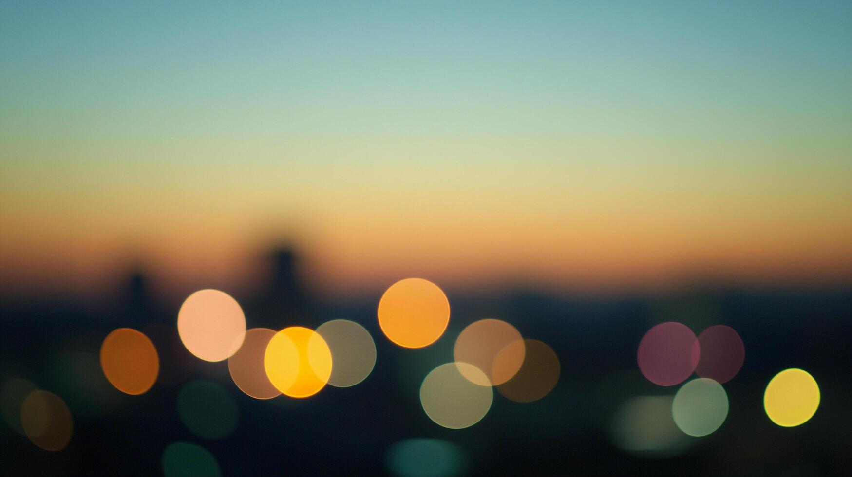 Blurred city lights glow softly against a warm sunset gradient sky, creating a dreamy and atmospheric abstract cityscape at twilight. photo