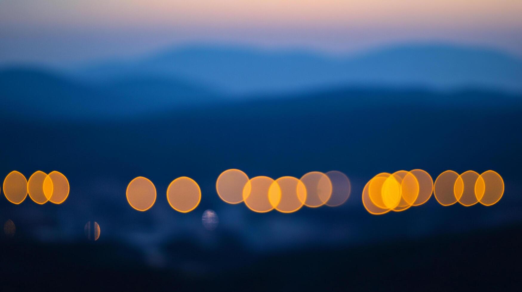 City lights blur in the night, painting a dreamy bokeh landscape against the backdrop of dark mountains and a twilight sky. photo
