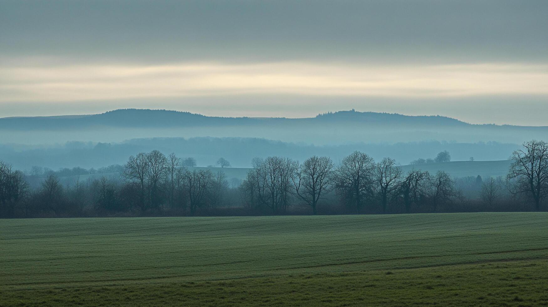 A misty landscape with fields and trees on a cloudy day, creating a serene and atmospheric scene in the countryside. photo