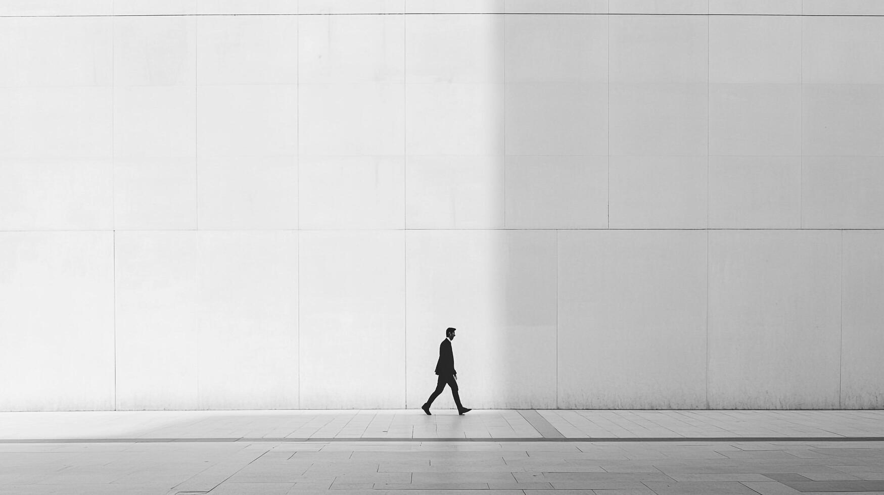 Solitary figure walking against a minimalist architectural backdrop, a study in light, shadow, and the dynamics of urban movement. photo