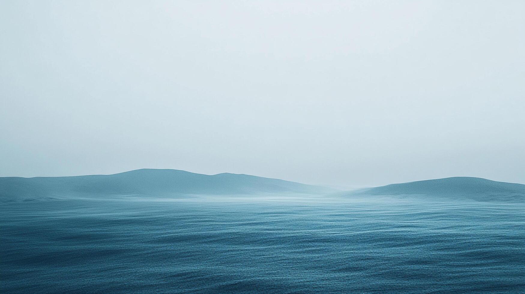 A misty seascape features gentle waves stretching to a distant horizon, with soft blue hues creating a tranquil and serene atmosphere. photo