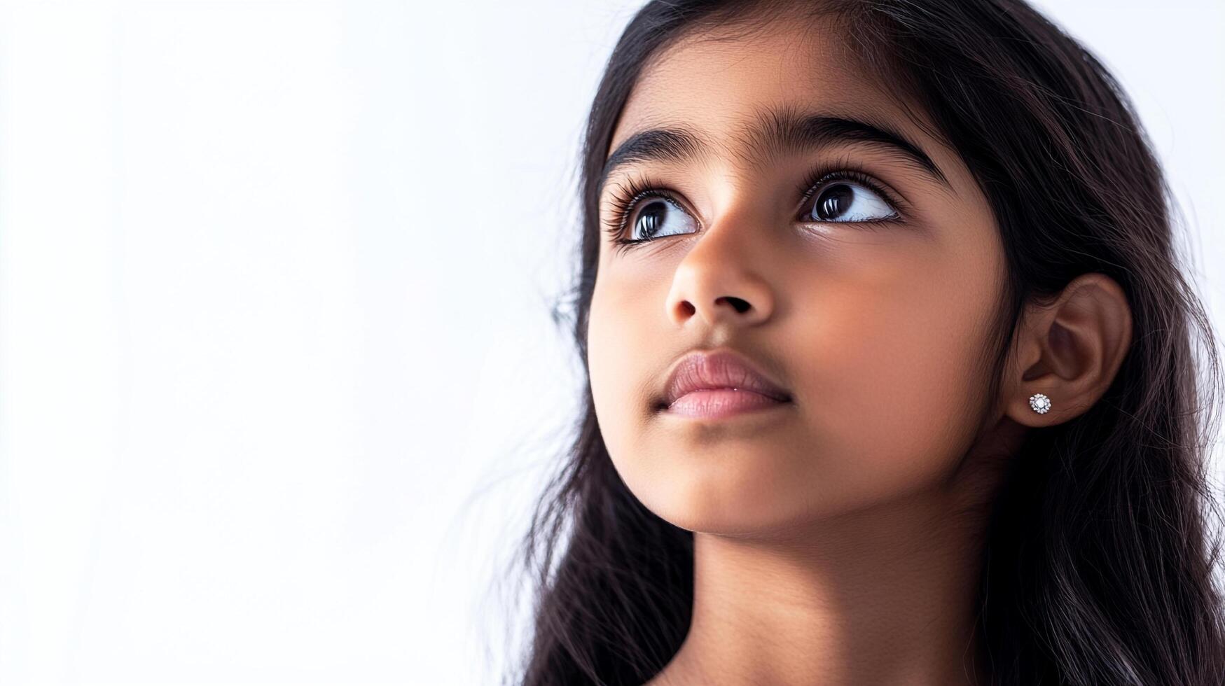 Young girl looks up with wonder, her dark hair cascading around her face, a small earring glinting against the light. Innocence captured. photo