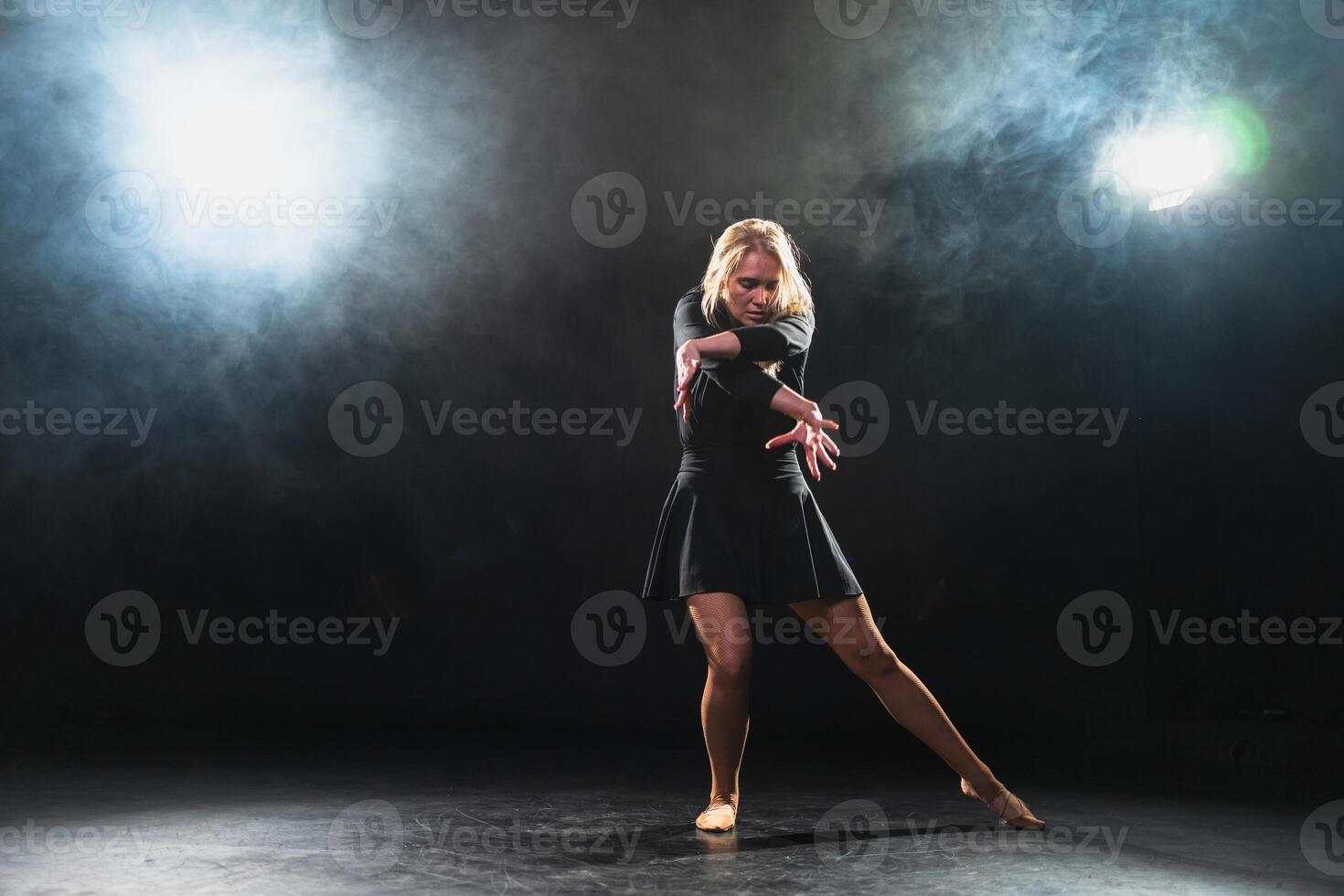 Contemporary woman dancer posing on black background with smoke. Adult female artist performer dancing with expression. Modern ballerina dancing in darkness. Passion dance in dark. Flexibility balance photo