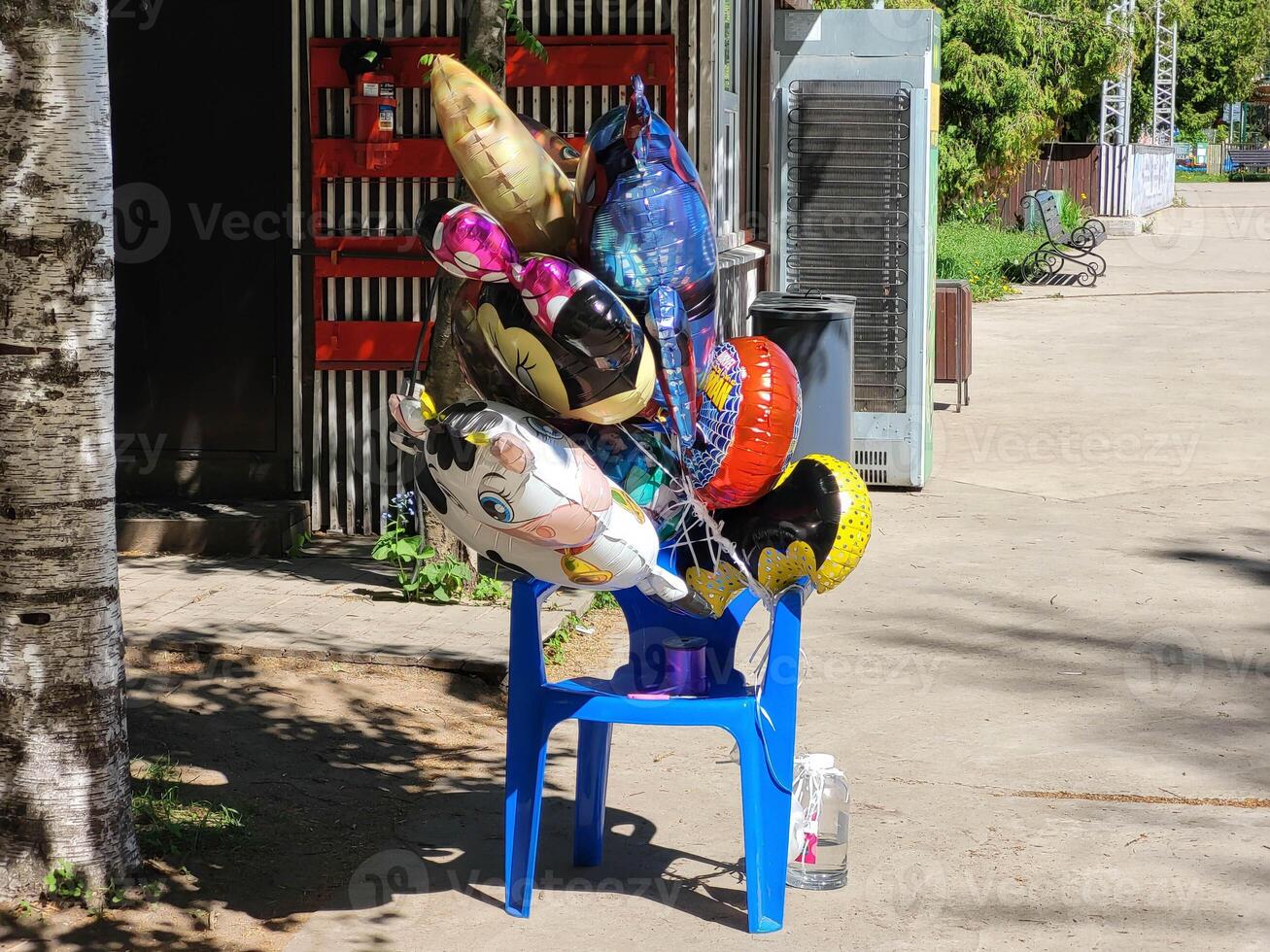A bunch of colorful helium balloons is tied to a blue plastic chair. photo