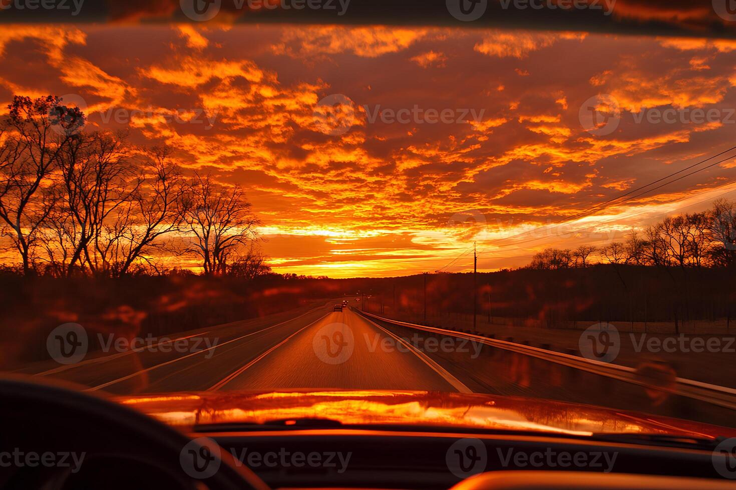 View from inside the car as it drives along a highway at sunset, with the warm colors of the sky reflecting through the windshield photo