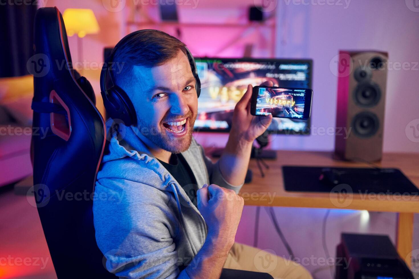 A man is sitting in a chair with headphones on and holding a controller photo