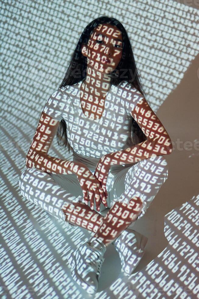 A woman sitting in front of a wall with words projected on it photo