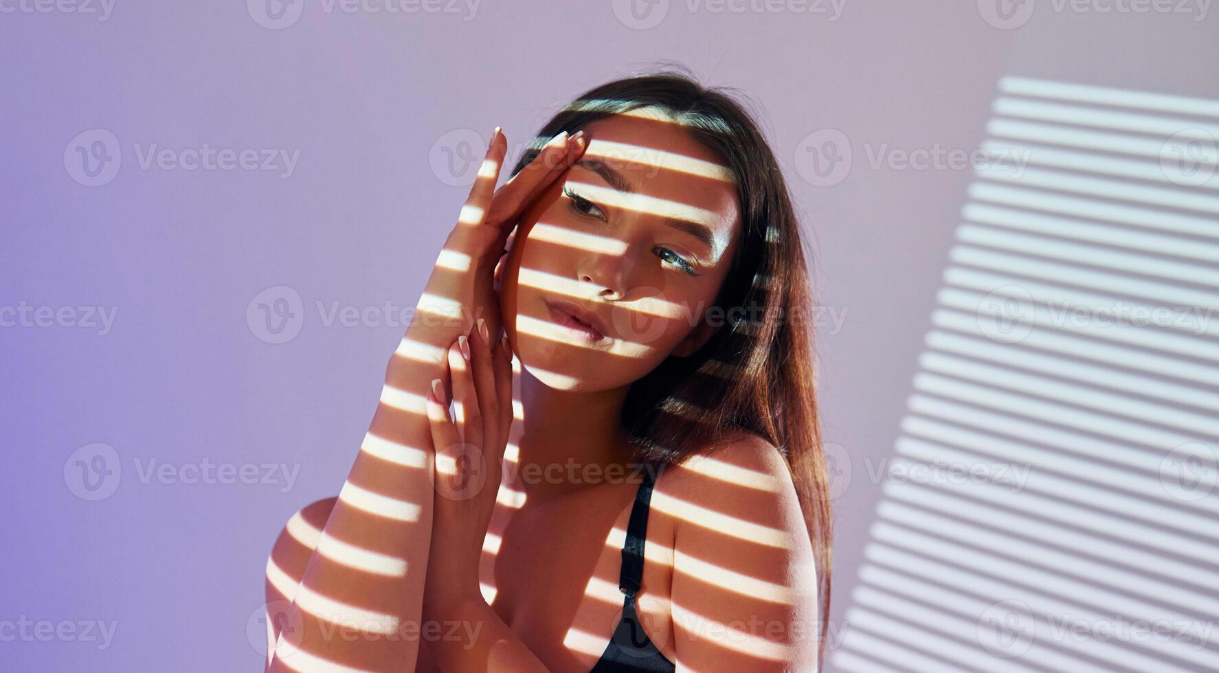 A woman is standing in front of a wall with a light shining on her photo