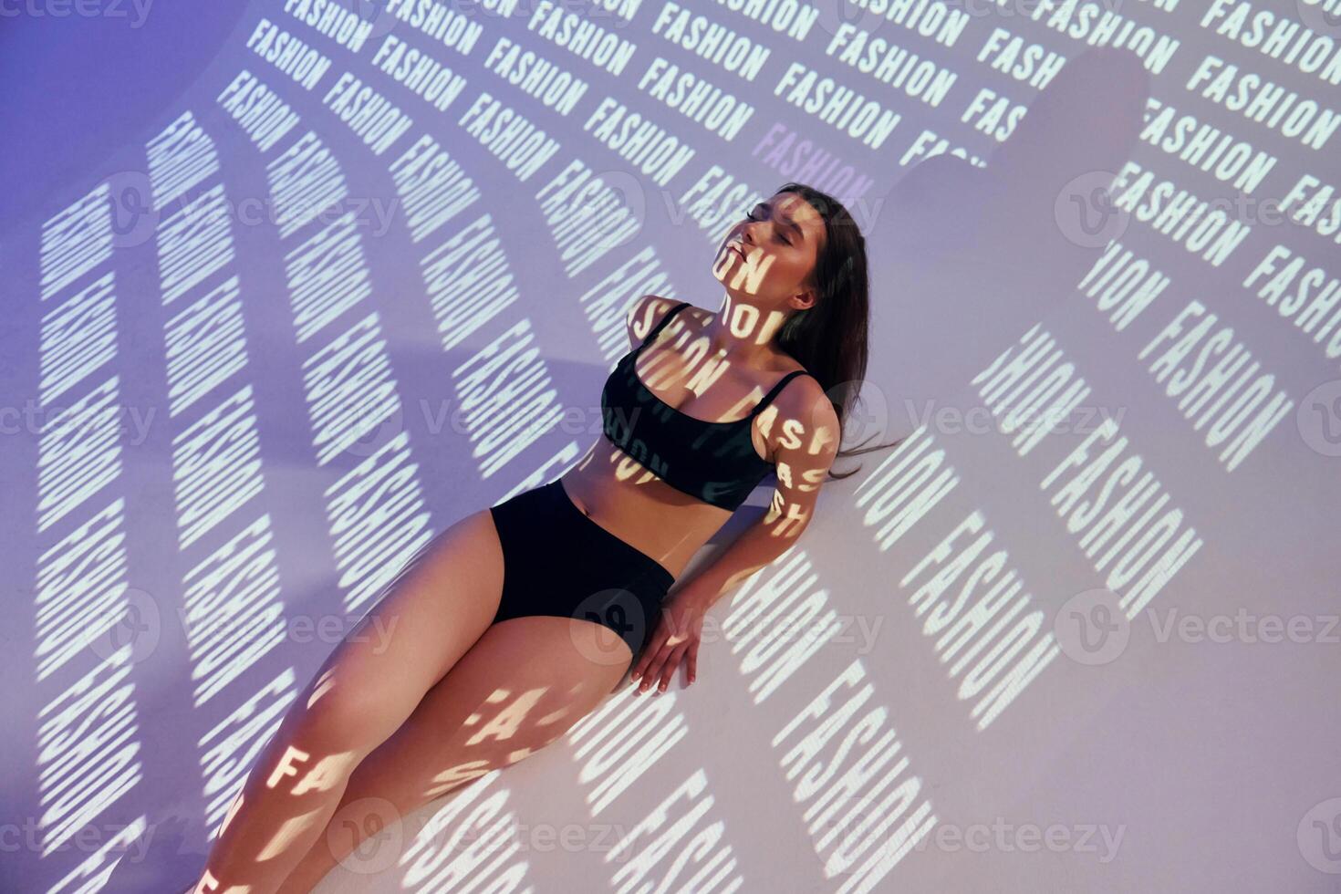 A woman in a black bikini top and underwear laying on a wall photo