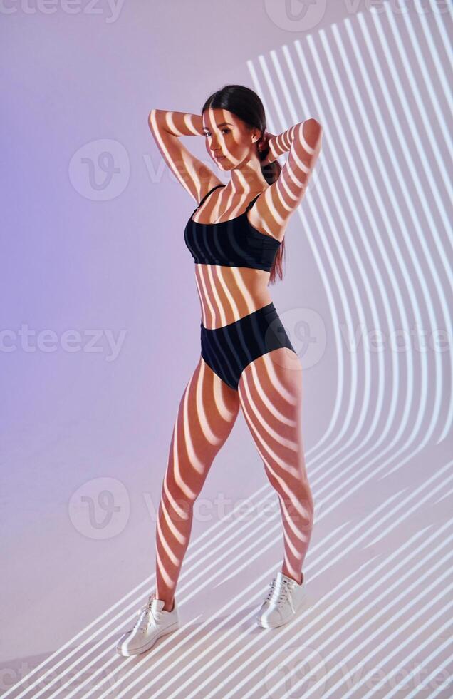A woman in a black bikini top and shorts standing in front of a light photo