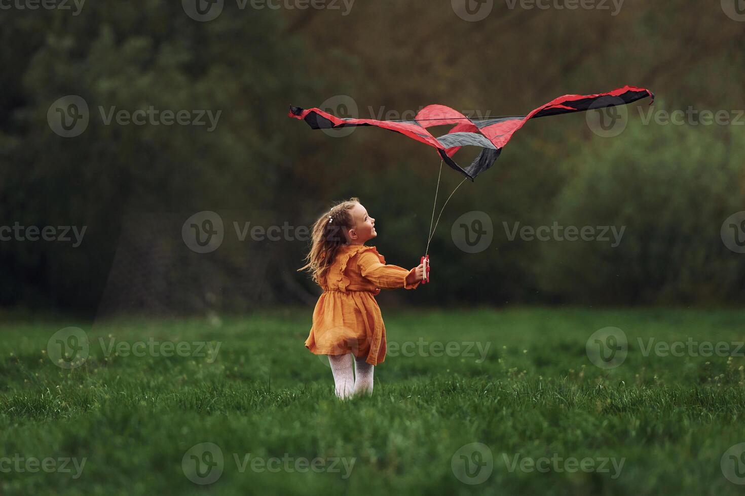 A little girl in a yellow dress is flying a kite photo