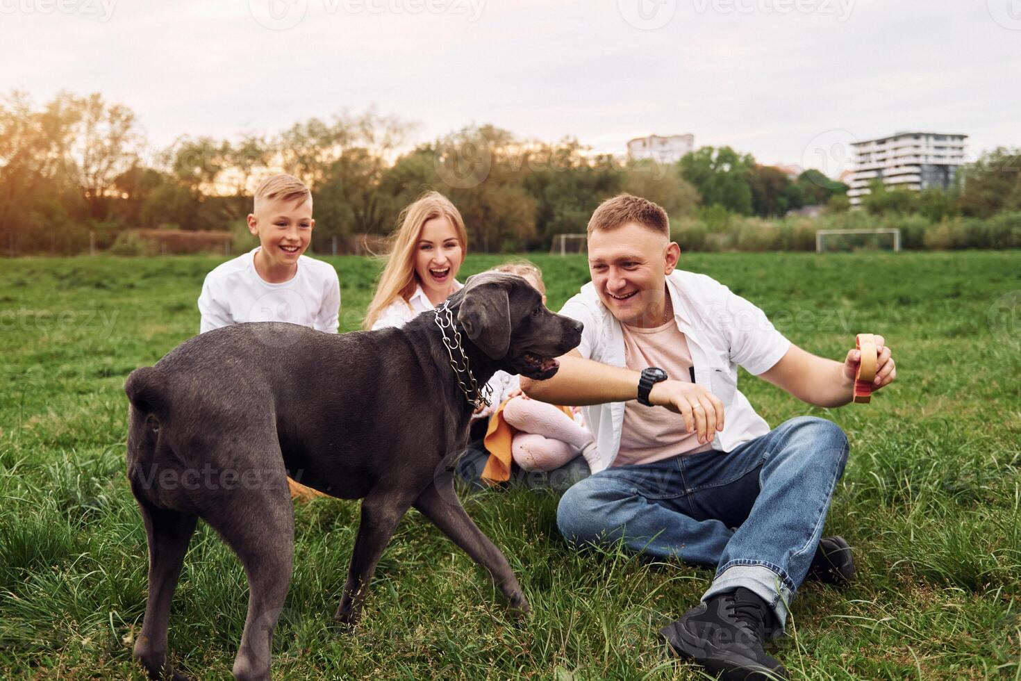 A family is sitting in the grass with a dog photo