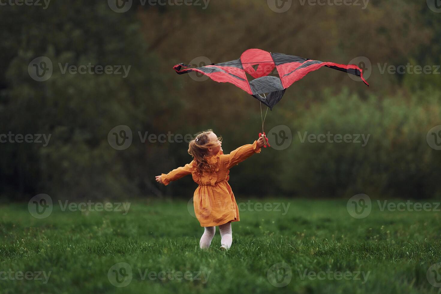 A little girl in a yellow dress is flying a kite photo