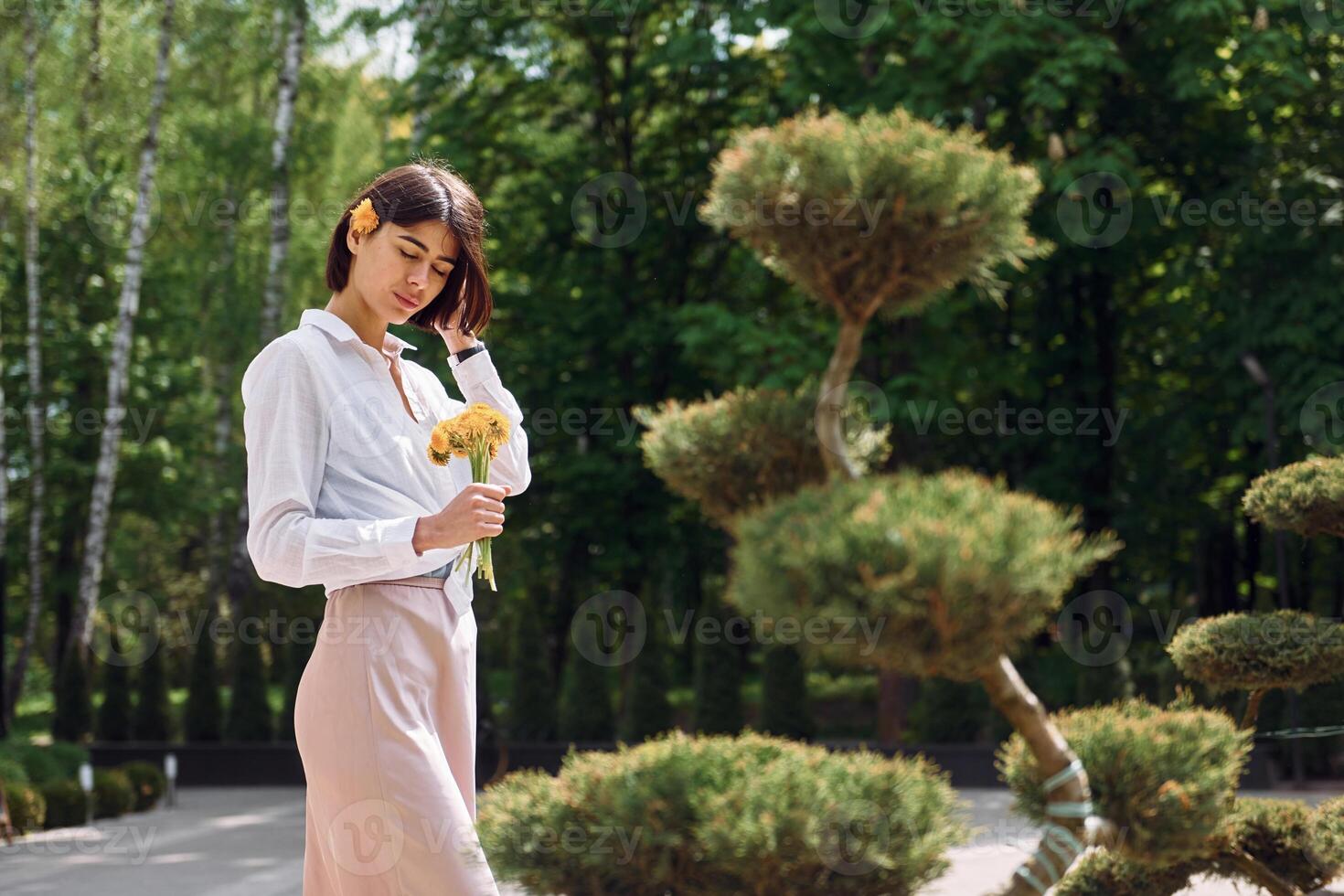A woman in a white shirt and pink skirt standing in front of a tree photo
