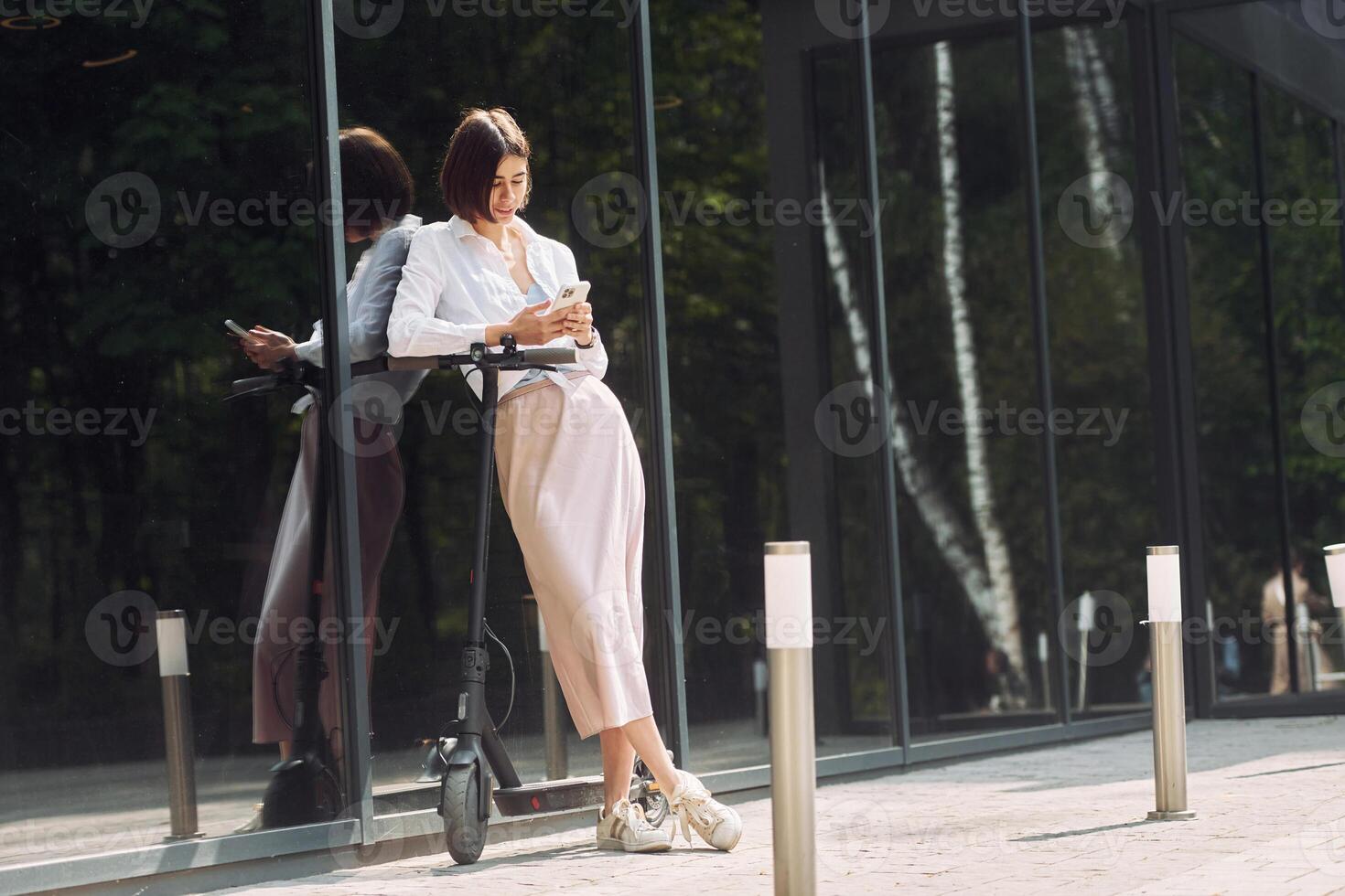A woman is leaning on a scooter while looking at her phone photo