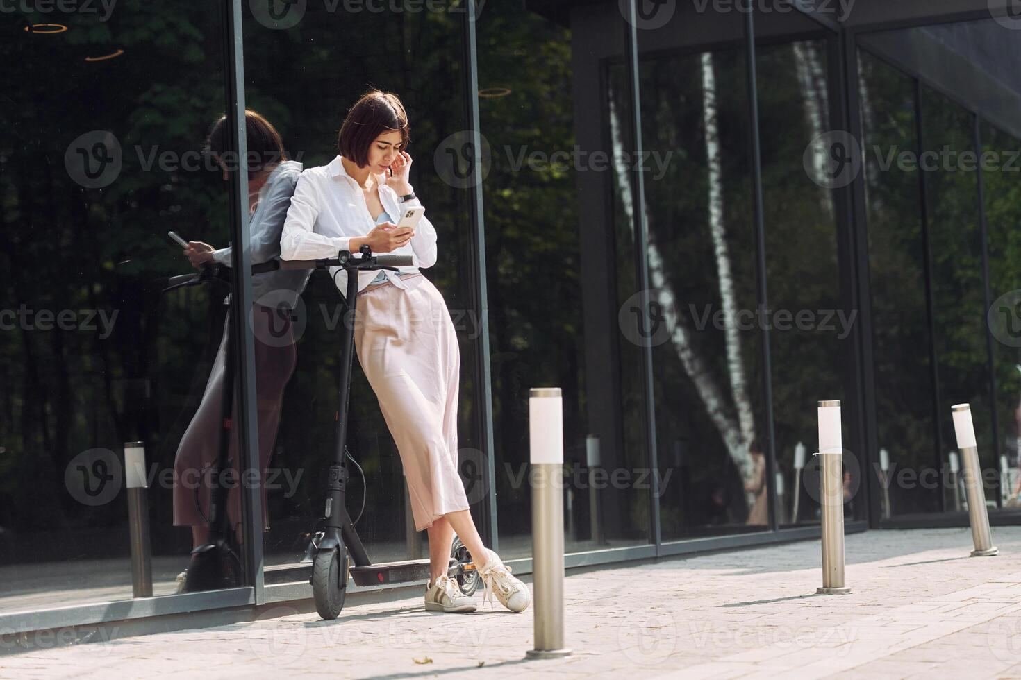A woman leaning against a wall while using her phone photo