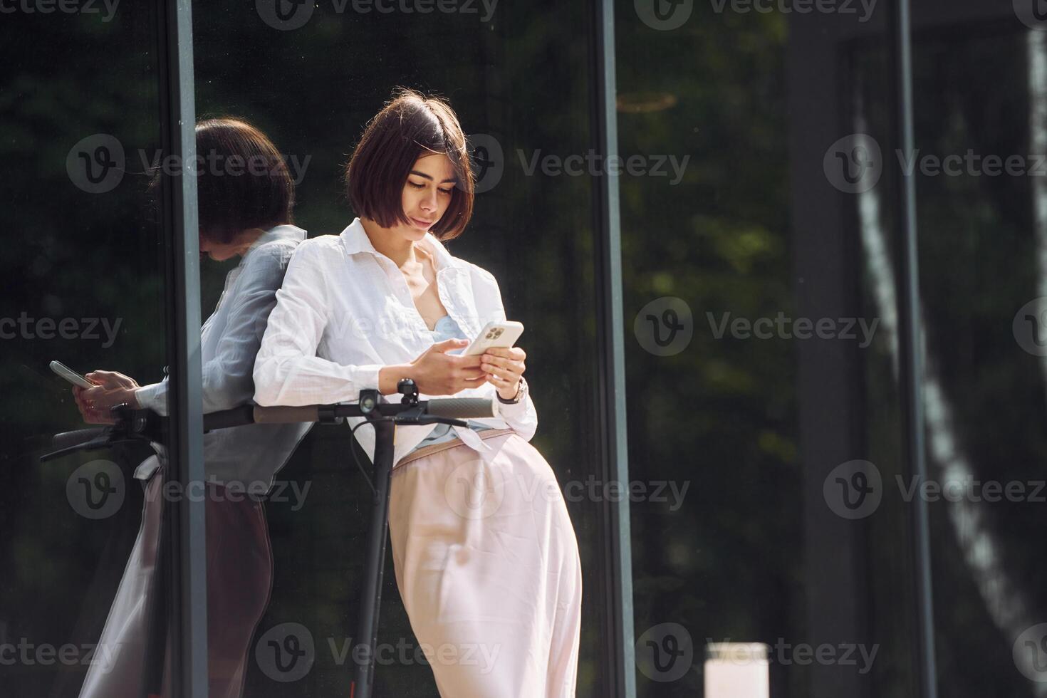 A woman in a skirt and blouse is looking at her phone photo