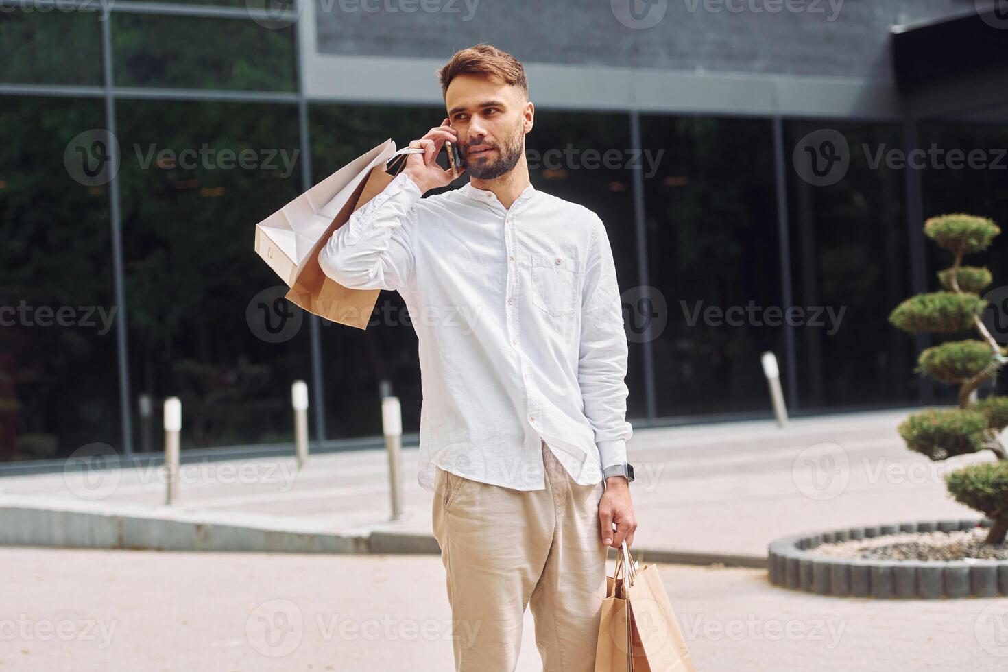 A man is holding shopping bags and talking on his cell phone photo