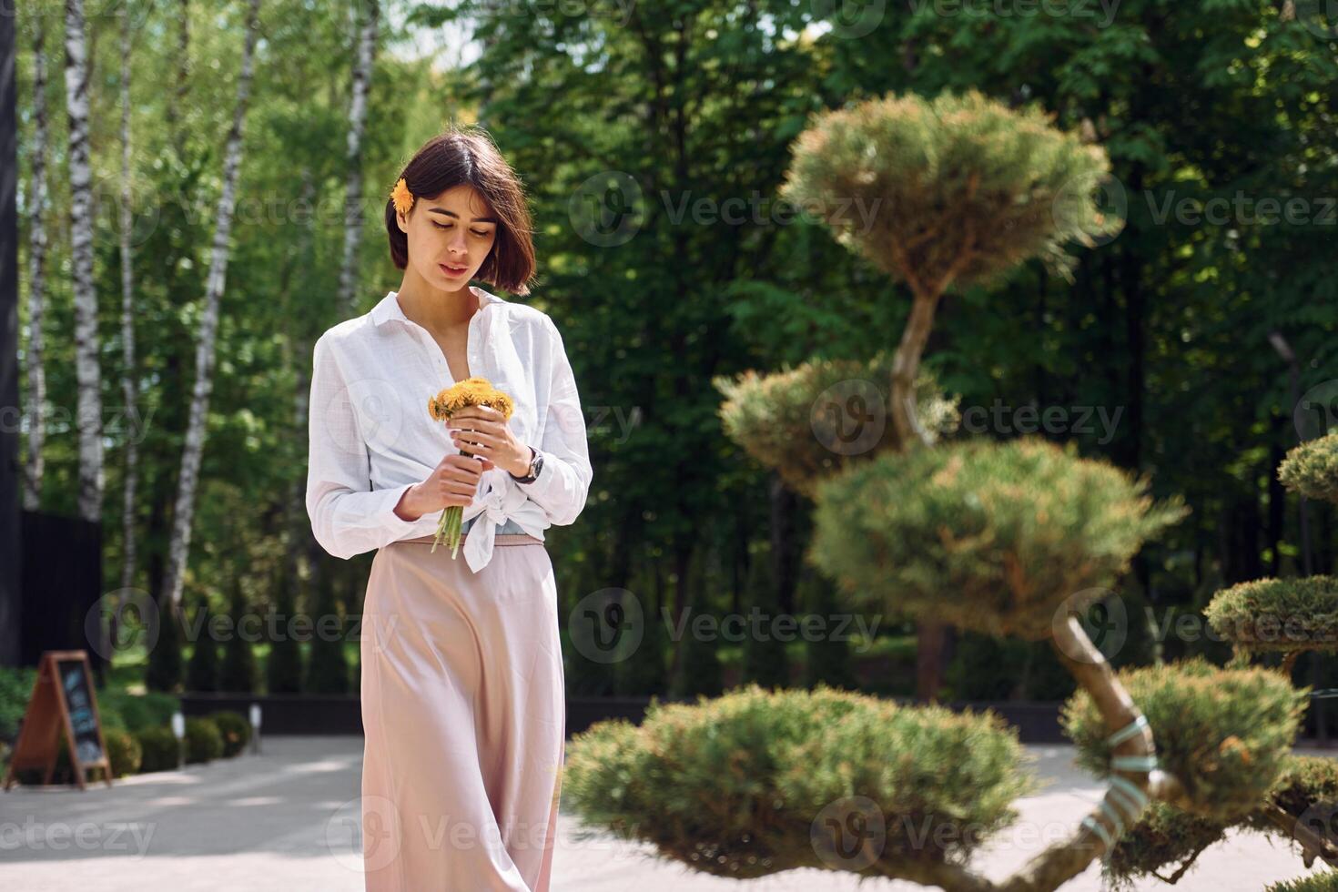 A woman in a white shirt and pink skirt standing near a tree photo