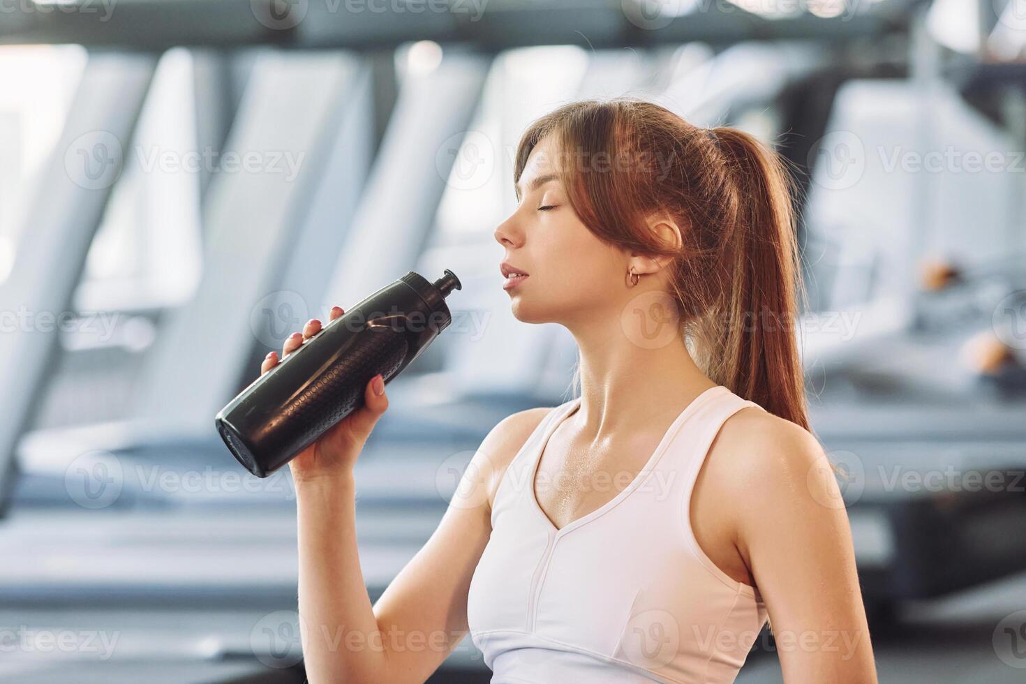 A woman drinking water from a bottle in a gym photo