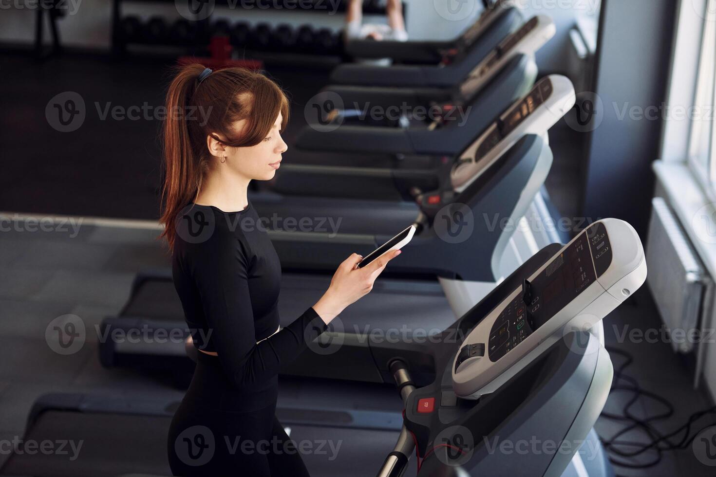 A woman is using her phone while on a treadmill photo