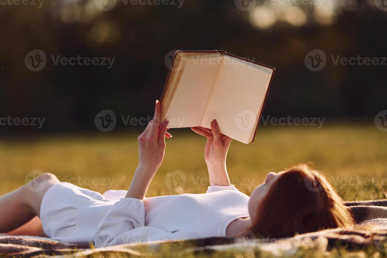 Holding the book.. Young girl is on the field at sunny daytime having nice weekend photo