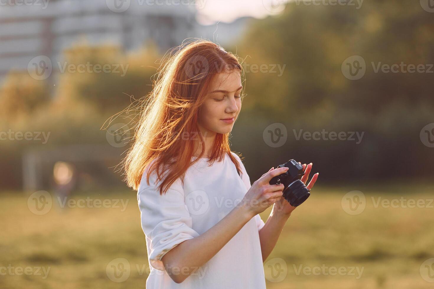 Photographers is with camera. Young girl is on the field at sunny daytime having nice weekend photo