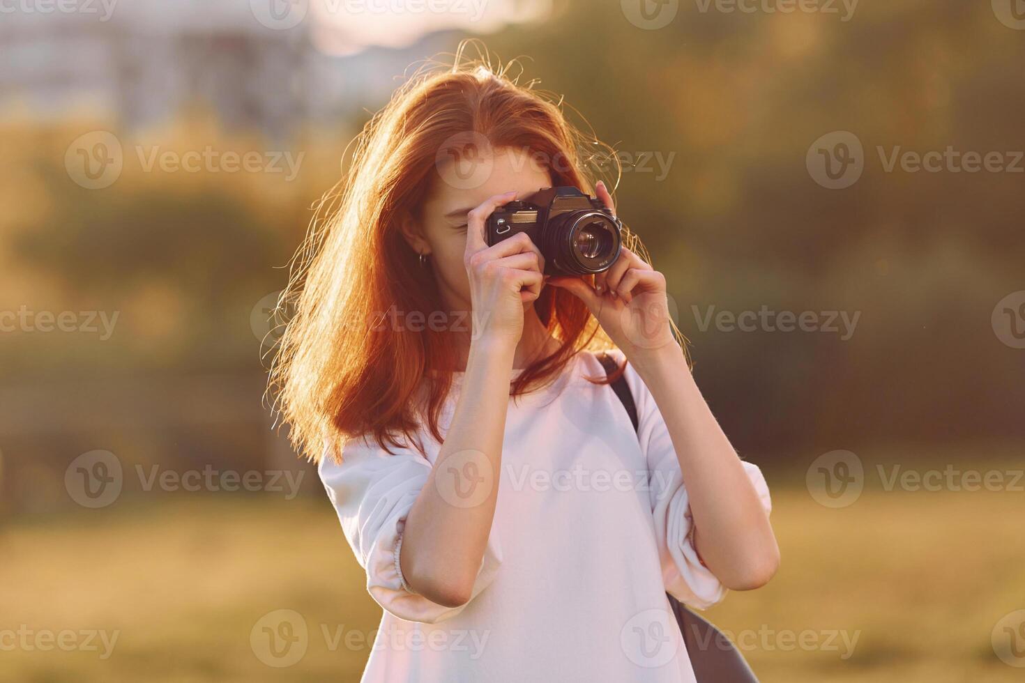 Photographer is with camerass. Young girl is on the field at sunny daytime having nice weekend photo