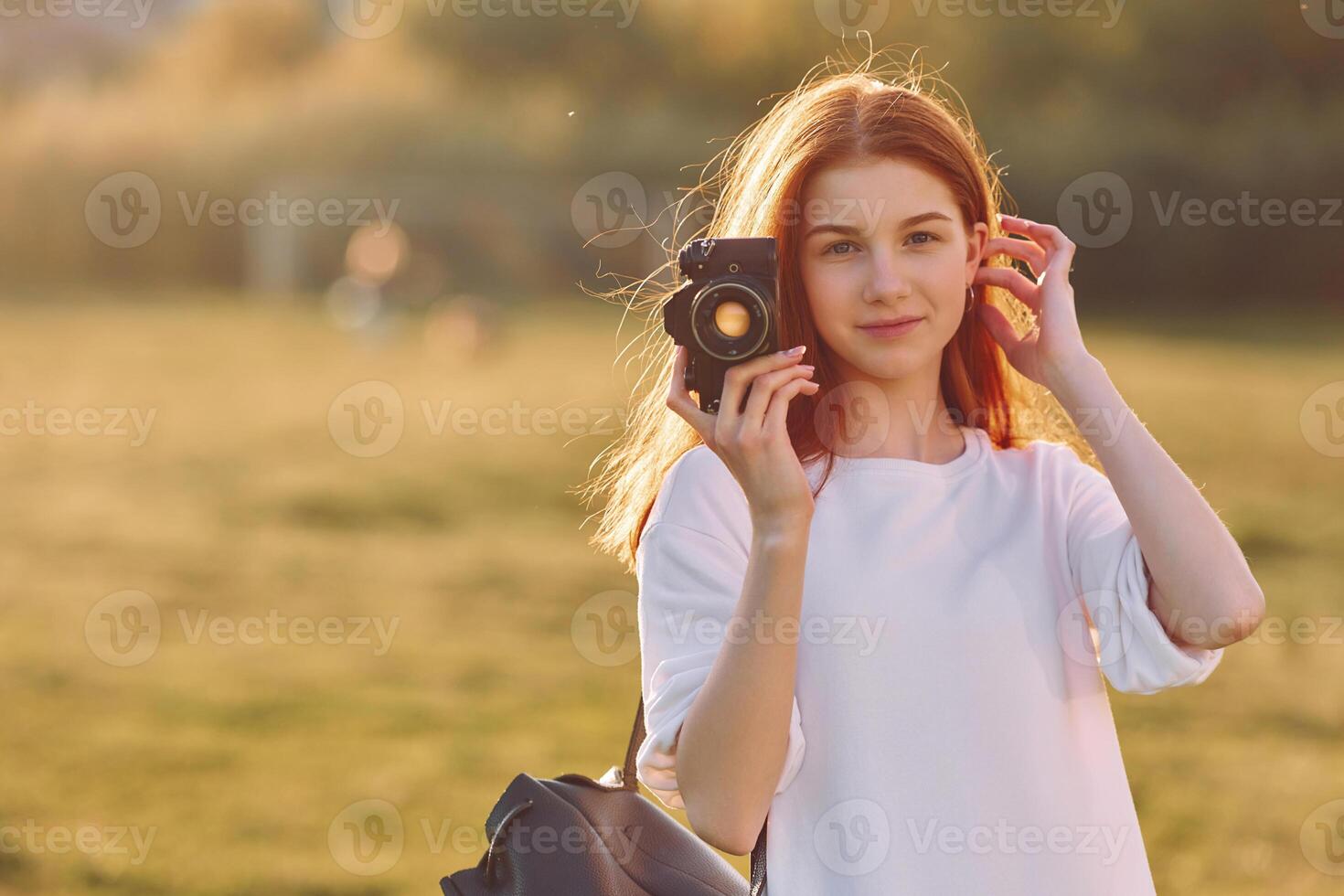 Professional camera in hand. Young girl is on the field at sunny daytime having nice weekend photo