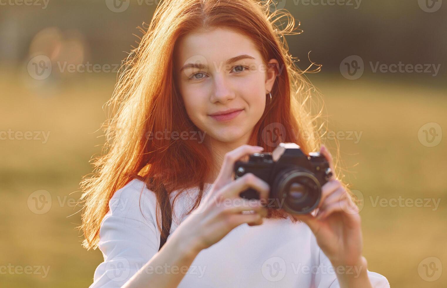 Holding camera. Young girl is on the field, at sunny daytime having nice weekend photo