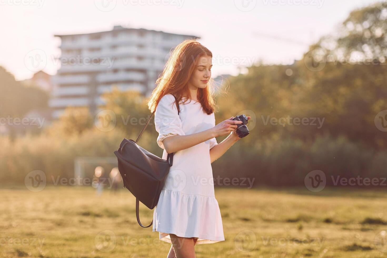 Professional camera in hands.. Young girl is on the field at sunny daytime having nice weekend photo