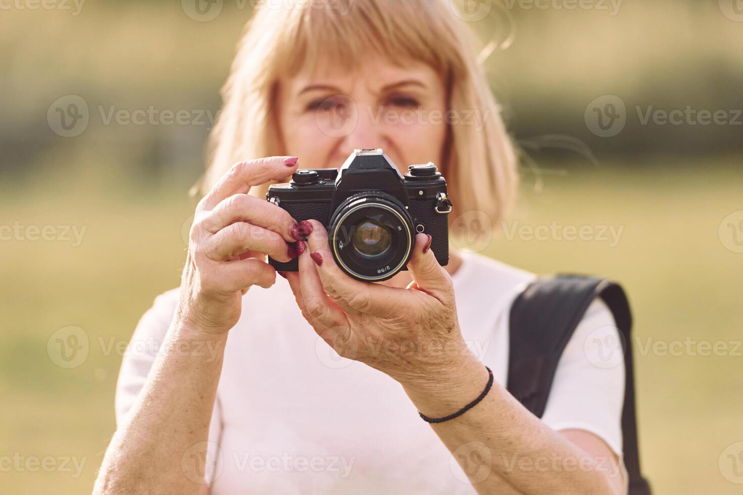 Using the camera,. Making the photos. Senior woman having nice weekend outdoors on the field at sunny day photo