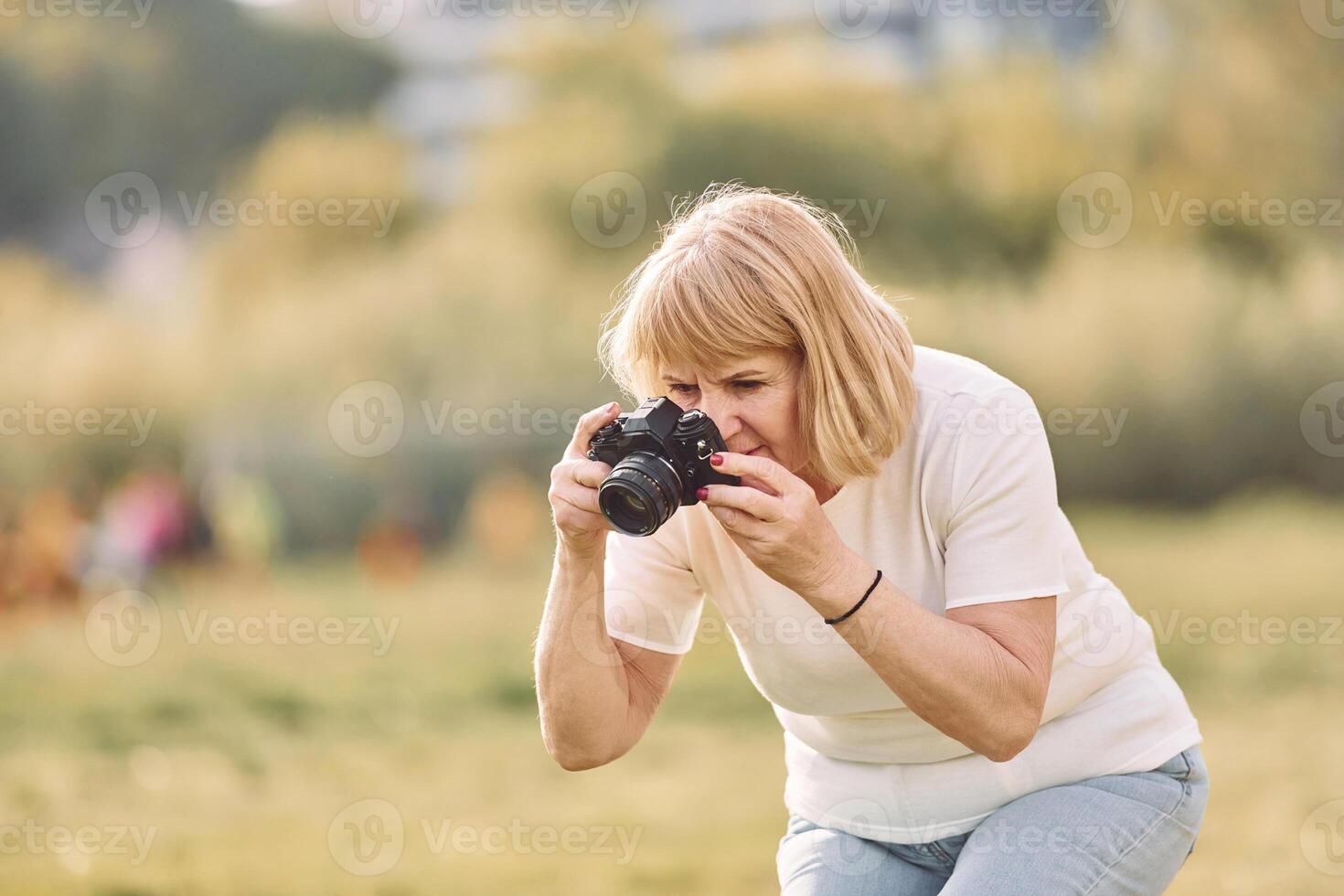 Photographer with a camera. ,.Senior woman having nice weekend outdoors on the field at sunny day photo