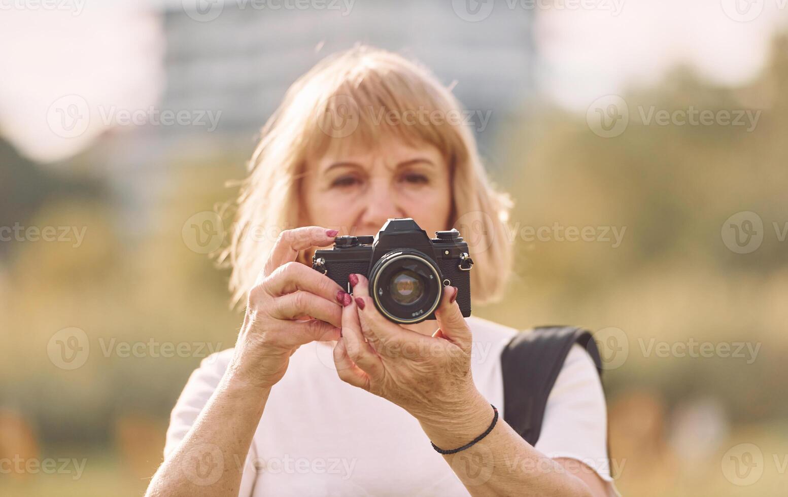 Using the camera. Making the photos.. Senior woman having nice weekend outdoors on the field at sunny day photo