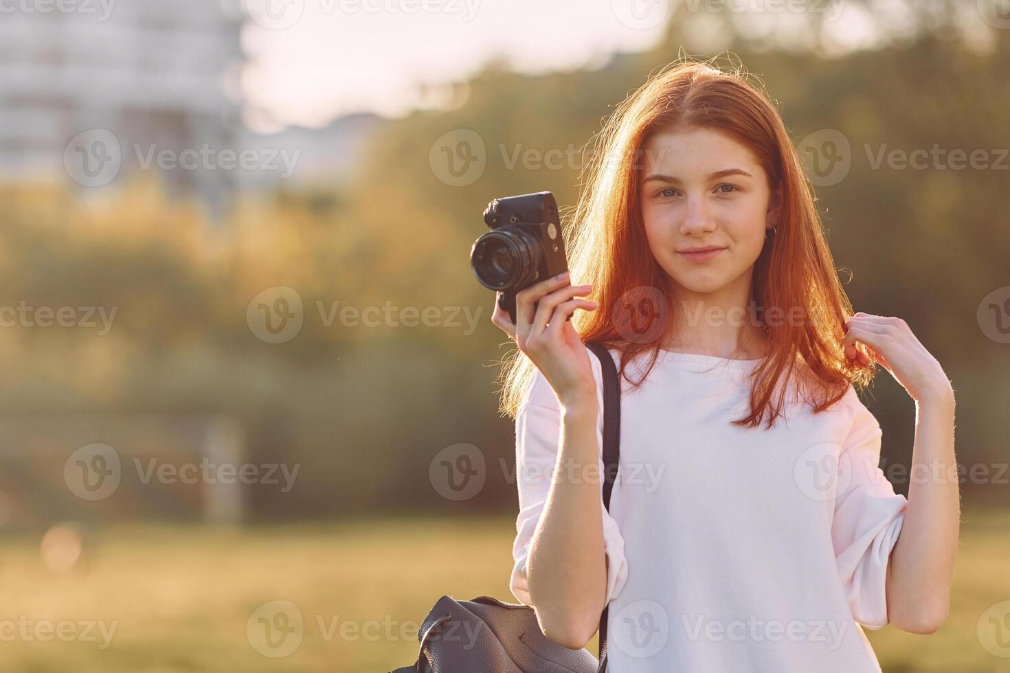 Professional camera in hands. Young girl is on the field at sunny daytime having nice weekend. photo