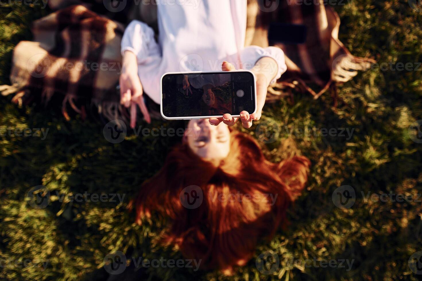 Laying down and making a selfie. Top view. Young girl is on the field at sunny daytime having nice weekend. photo