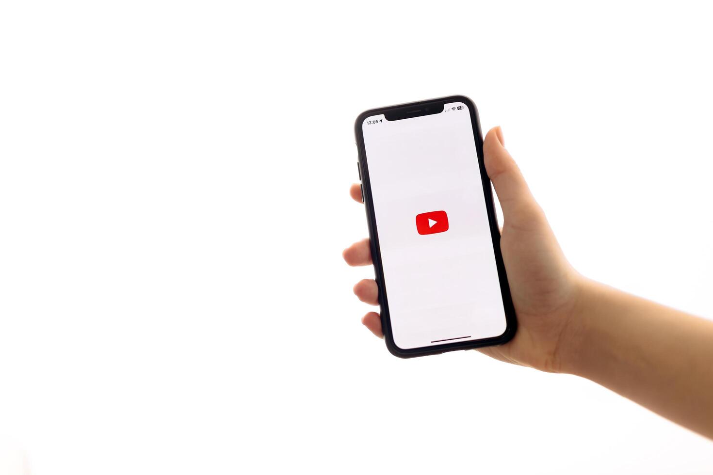 Zaporizhia, Ukraine - January 10, 2025. A woman holds an iPhone with the YouTube app logo on the screen while using a mobile app for business at home. white background photo
