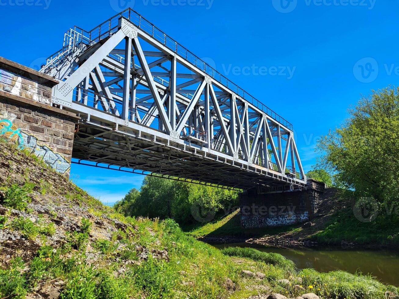 On a clear sunny day, there is a small railway bridge over a small river photo