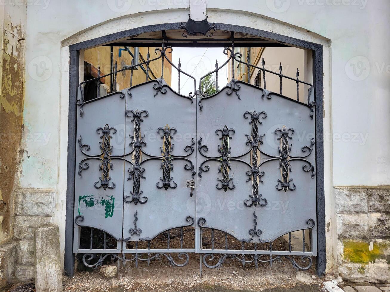 The arch of the house has a grey iron gate with wrought iron elements photo