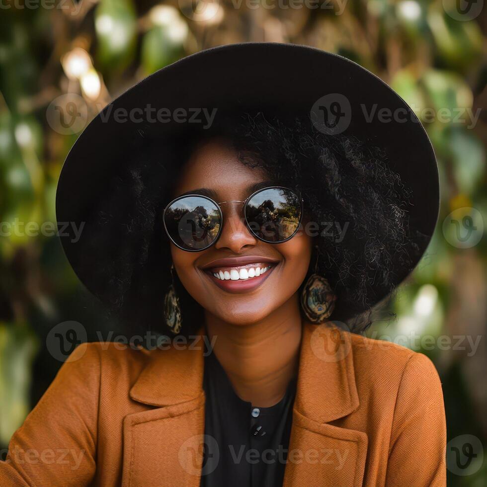 A smiling woman with an afro wearing sunglasses and a hat photo