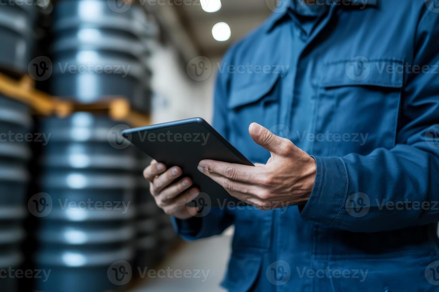 Worker uses tablet to check inventory in a warehouse filled with barrels during the day photo